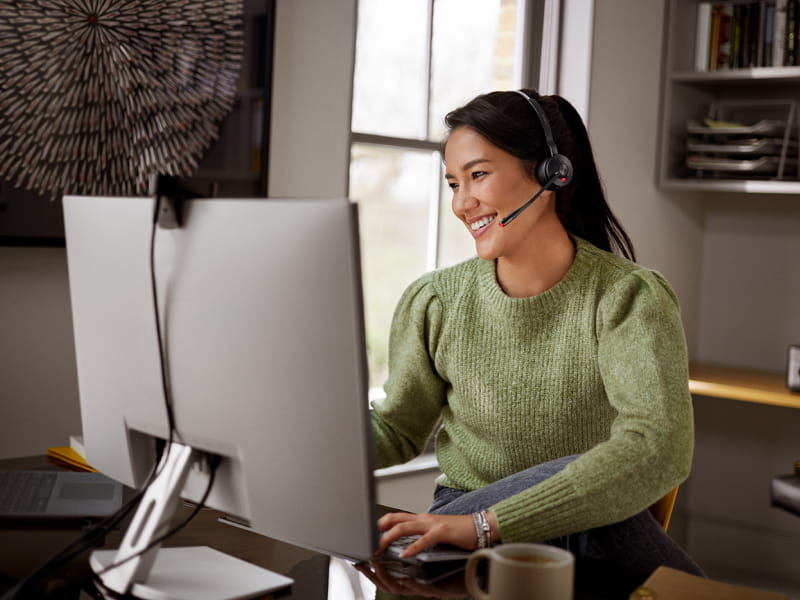 Person wearing a headset, typing at a large monitor in a home offic