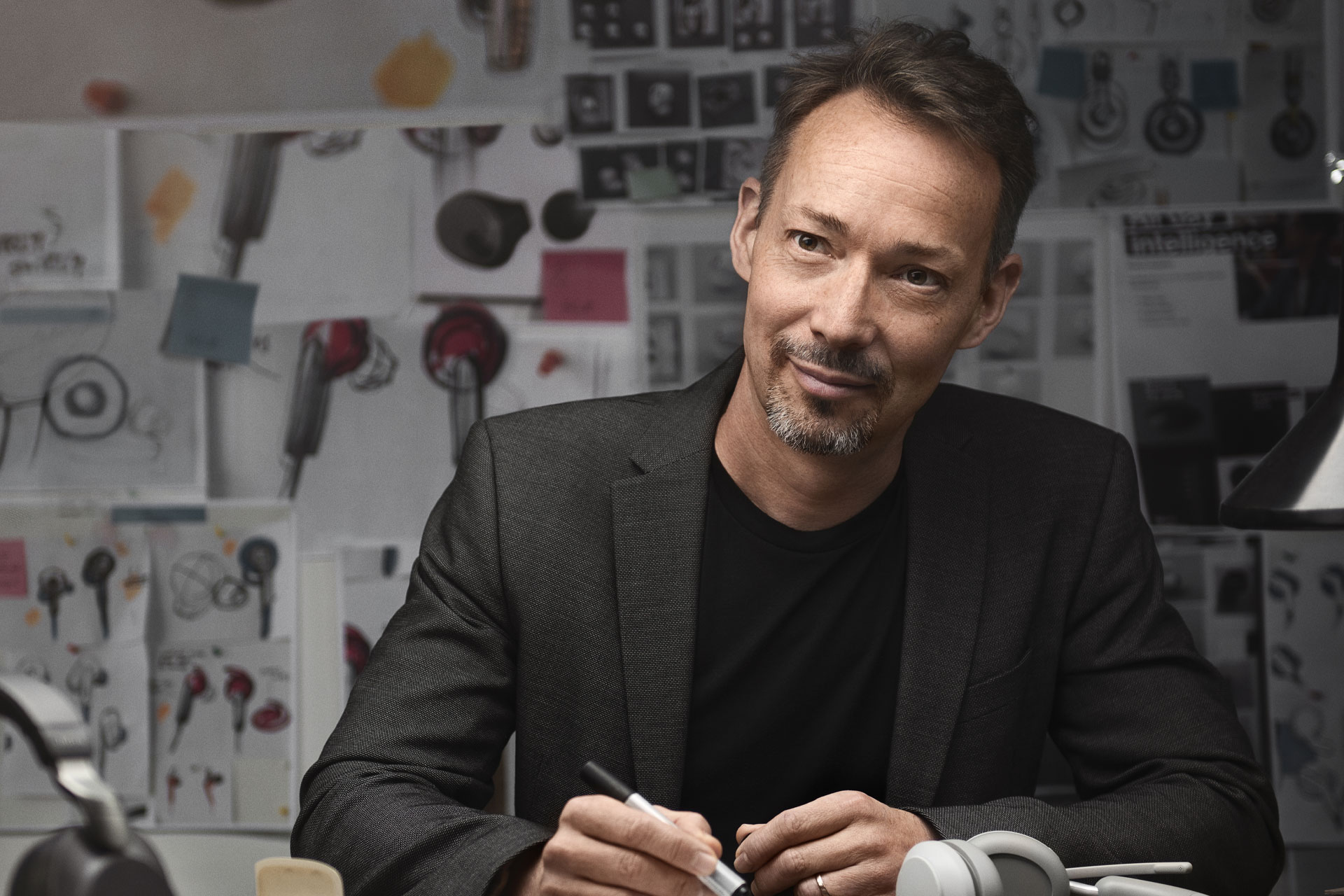 Person in a dark blazer at a desk with audio equipment sketches in the background.