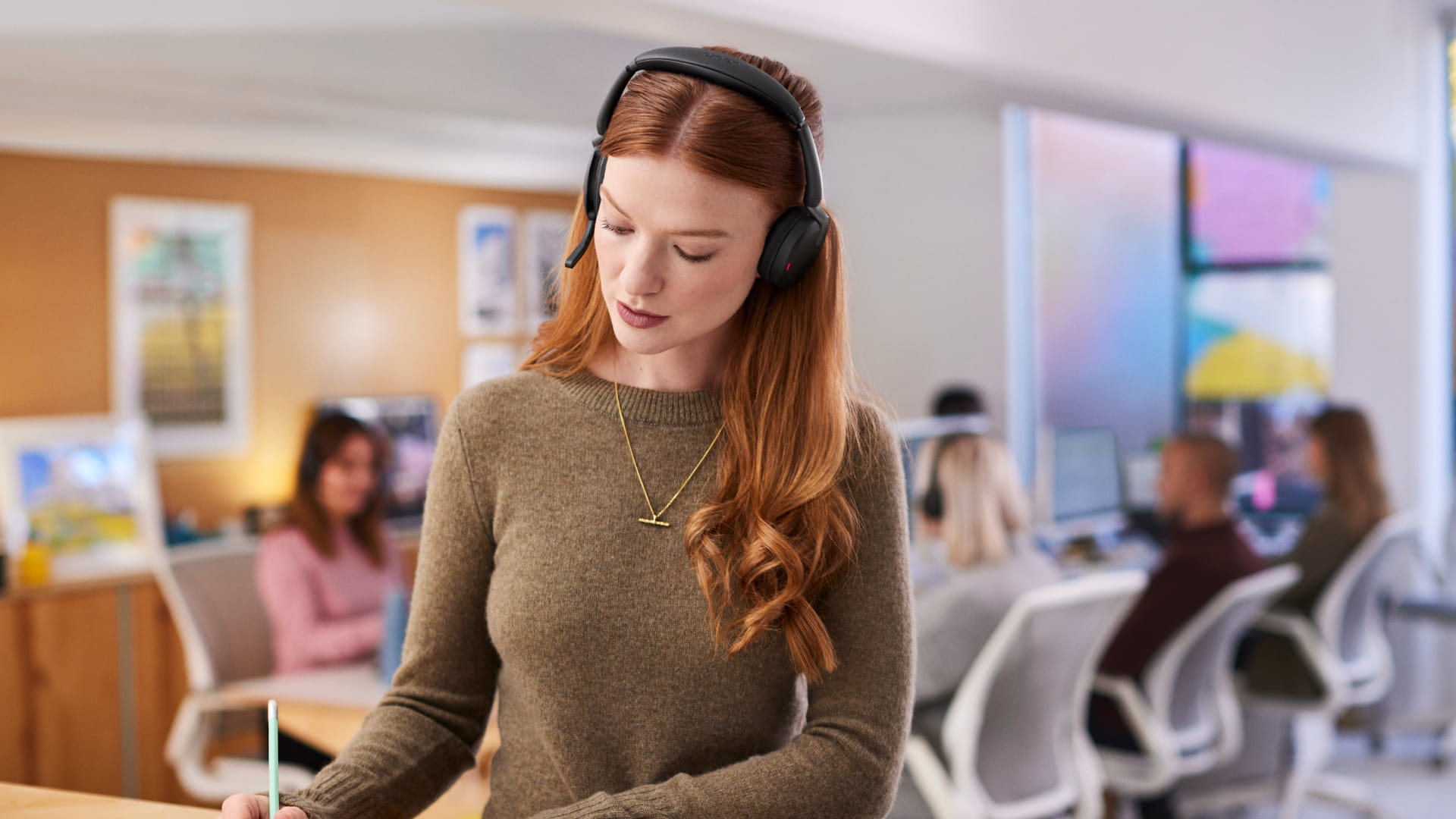 Woman wearing Jabra Evolve2 65 Flex headset at work in an open-plan office – ideal headset for hybrid working with ANC