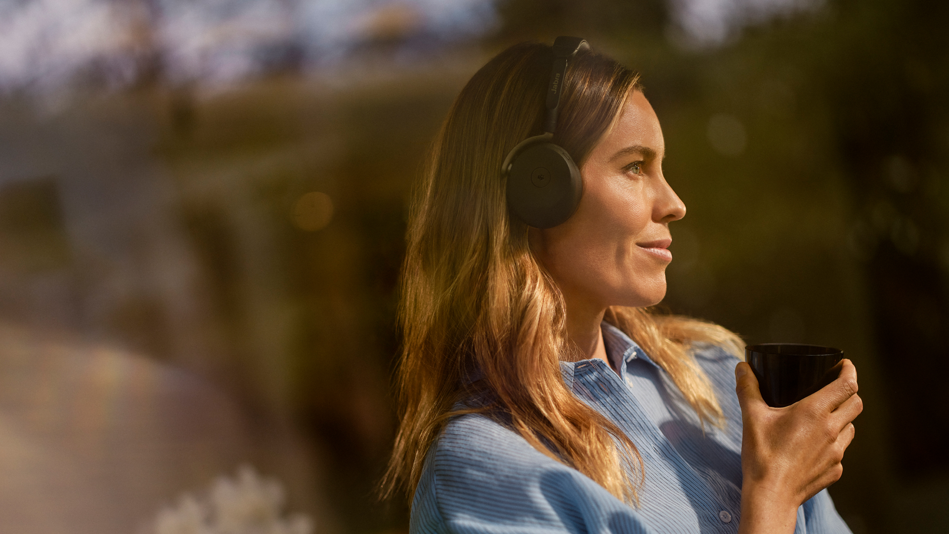 Person wearing Jabra Evolve3 65 Flex headset while holding a mug