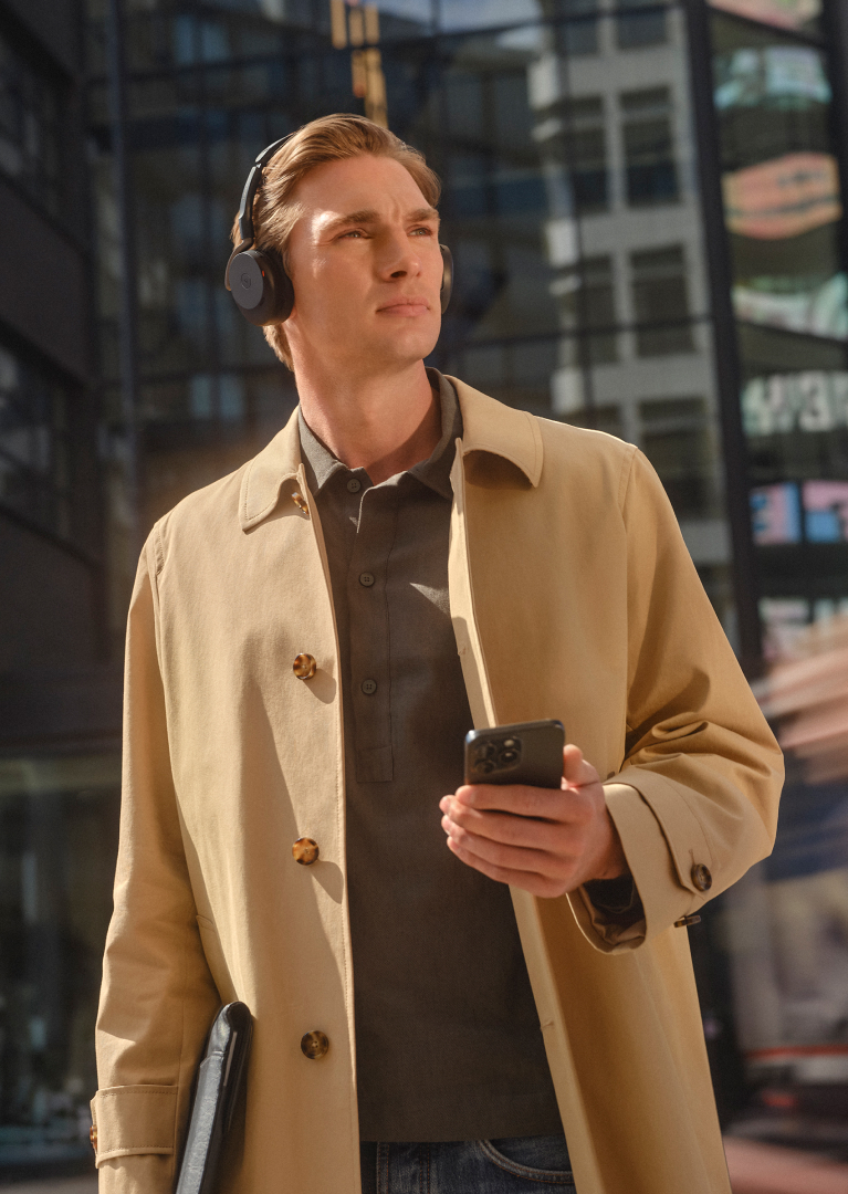 Person in beige jacket wearing Jabra Evolve3 65 Flex headset while holding a mobile phone